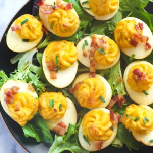 Smoked deviled eggs arranged on a wooden platter, garnished with paprika and chives, showcasing their golden, creamy filling and a subtle smoky flavor.