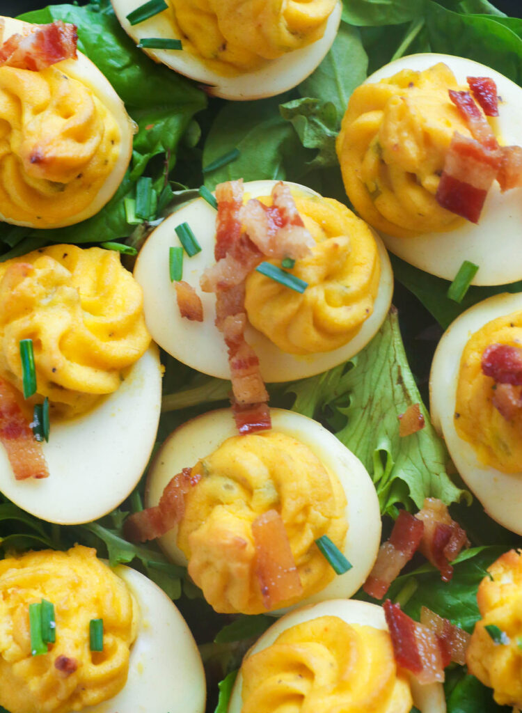 Deviled eggs arranged on a wooden platter, garnished with paprika and chives, showcasing their golden, creamy filling and a subtle smoky flavor.